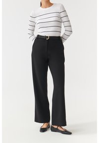 Weißes Langarmhemd mit schwarzen horizontalen Streifen, kombiniert mit hochtaillierten schwarzen Hosen und schwarzen flachen Schuhen, minimalistisches Design.