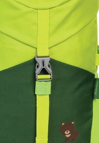 Un sac à dos vert et jaune vif avec une texture durable, doté d'une boucle grise et d'un petit motif d'ours près du bas.