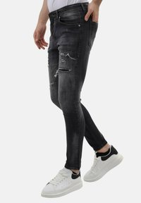 Zwarte skinny jeans met versleten details en rafelige stukken, gecombineerd met witte sneakers met een zwart accent op de hak en een textuur sole.