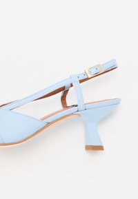 Svetlo modré slingback podpätky so zatvorenou špičkou, nastaviteľným popruhom a blokovým podpätkom. Vrchný materiál je hladká koža s jemnými švovými detailmi.
