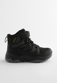Botte de randonnée noire imperméable avec tige haute, lacets à l'avant, bande Velcro et semelle épaisse à crampons pour usage extérieur.