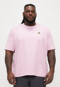 Tricou scurt cu mânecă, de culoare roz deschis, cu guler rotund, croială lejeră, prezintă un mic logo brodat cu fluture galben în partea stângă a pieptului.