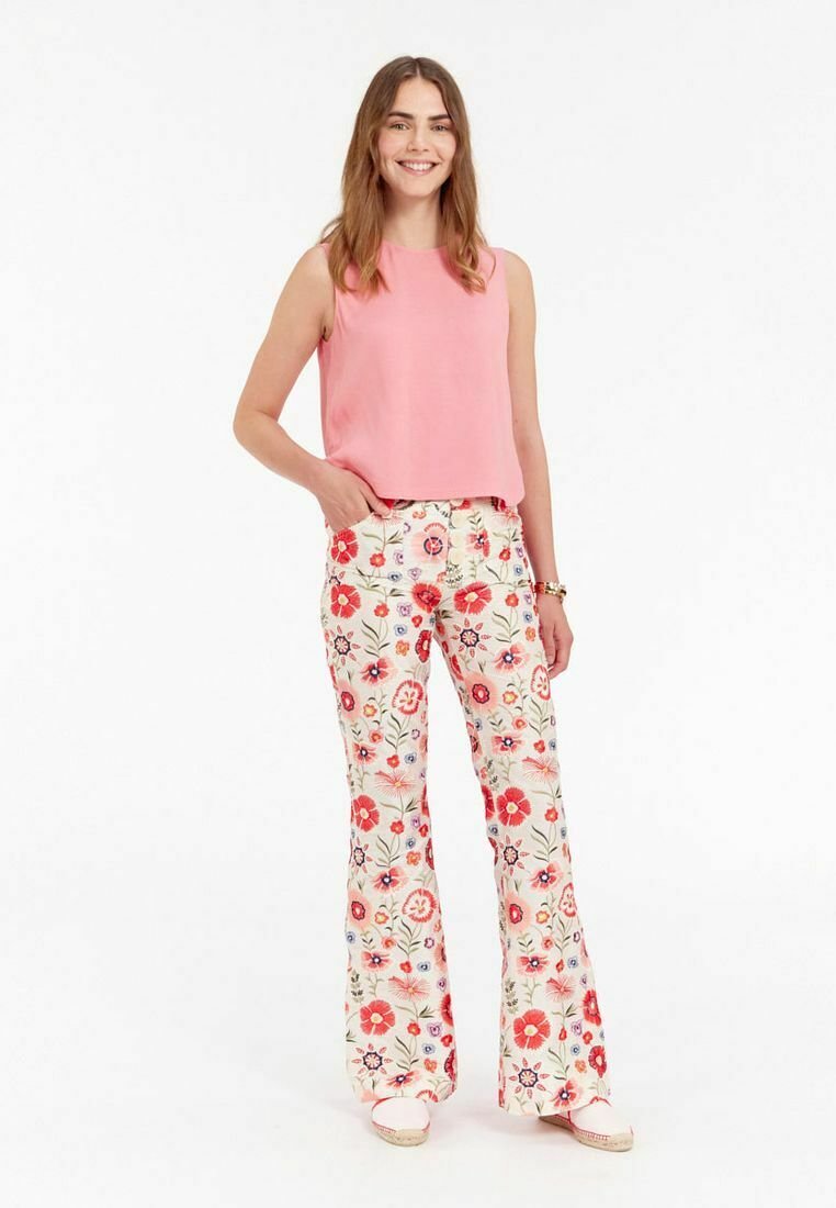Haut sans manches rose associé à un pantalon évasé à motifs floraux en crème, avec des fleurs rouges et bleues, et des espadrilles blanches.