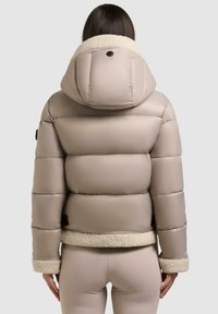 Puffige beige Jacke mit einem strukturierten, cremfarbenen Kunstpelzkragen und -manschetten, mit Kapuze und elastischem Saum, von hinten betrachtet.