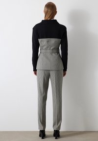 Conjunto de blazer y pantalones a medida en negro y gris con cuadros, que presenta una cintura ceñida, diseño estructurado y tejido suave. Se pueden ver zapatos de tacón alto.