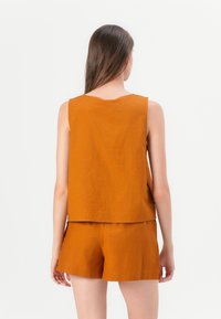 Rostfarbener, ärmelloser Oberteil mit rundem Ausschnitt, kombiniert mit passenden kurzen Bottoms. Beide haben eine glatte Textur und eine lockere Passform.