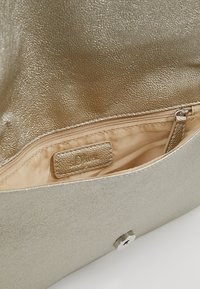 Borsa in metallo dorato con un'esterno testurizzato, caratterizzata da un interno beige e una tasca con zip. La chiusura è un bottone a pressione argentato.