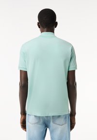 Polo shirt verde menta chiaro con maniche corte, texture liscia e colletto classico, visto da dietro. Indossato con jeans di denim blu.