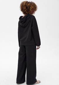 Czarna, oversize bluza z kapturem, z przednią kieszenią i sznurkiem; w połączeniu z szerokimi czarnymi spodniami. Na nadgarstkach widoczne paskowane mankiety.