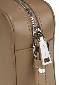 Borsa in pelle beige con una cerniera argentata dotata di un cursore dettagliato e cuciture visibili lungo i bordi per un'aggiunta di texture.