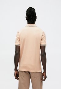 Rövid ujjú polo ing puha őszibarackszínű anyagból, kontrasztos szegéllyel ellátott gallérral és laza szabással, bézs bordázott nadrággal párosítva.