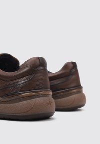 Zapatillas de piel marrón con suelas acolchadas, tacones redondeados y detalles de costura sutiles. Acabado texturizado y diseño de perfil bajo.