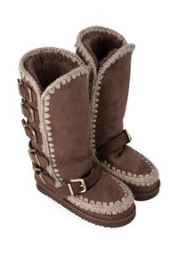 Stivali in suede marrone con un design alto, caratterizzati da cuciture decorative, un bordo intrecciato e fibbie metalliche lungo il lato per una vestibilità regolabile.