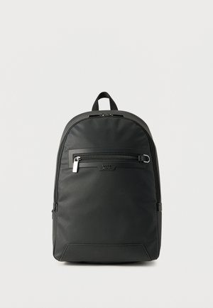 Črni teksturirani nahrbtnik z žepom z zadrgo spredaj, zgornjim nosilnim trakom in minimalnim logotipom na preprostem belem ozadju.