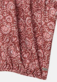 Tissu rouge avec un motif floral en rose et bleu clair. Ourlet froncé avec une petite étiquette argentée portant l'inscription "Pacific Republic". Surface texturée.