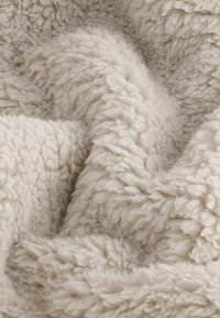 Rakenne beige fleece-materiaali, jossa on pehmeä ja pörröinen pinta, osoittaa kerroksellisia taitoksia ja tiheää, kiharaa kuitumallia.