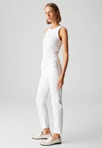 Witte tanktop en strakke witte jeans. Glad, lichtgewicht materiaal. Casual instapschoenen in crème met textuurelementen. Neutrale achtergrond.