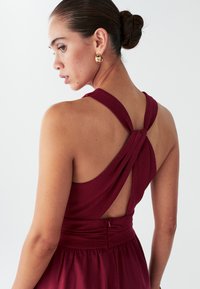 Burgundia värvi kleit tekstuurse kangaga, millel on seljal ristuvad sangad ja liibuv vöökoht. Nähtav luku detail.