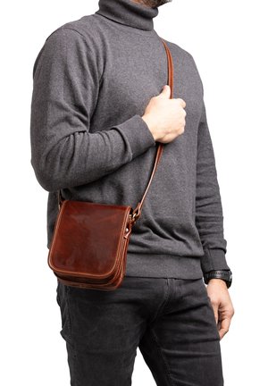 Borsa a tracolla in pelle marrone con forma quadrata, cuciture chiare a contrasto e tracolla regolabile, indossata a spalla.