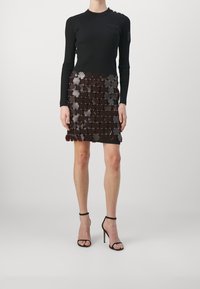 Svart ribbad långärmad topp med en figurnära silhuett, ihop med en lager-på-lager kort kjol gjord av reflekterande blomformade element i mörkbrun.