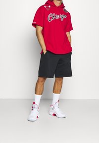 Sudadera con capucha roja que lleva el texto "Chicago", pantalones cortos negros, zapatillas deportivas blancas y rojas, y calcetines blancos, mostrando un atuendo deportivo casual.