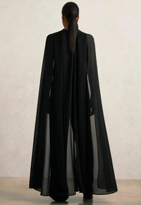 Černé, průsvitné šaty s pláštěm a dlouhými, splývavými rukávy a vysokým výstřihem. Má hladkou strukturu a elegantní siluetu.
