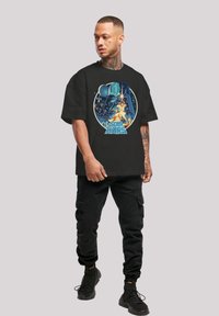 Camiseta de algodón negra con un estampado gráfico de un personaje y texto de Star Wars, mangas cortas, corte relajado, escote redondo.