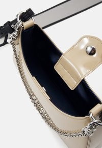 Beige lakatunahkainen käsilaukku, jossa on hopeinen ketjuyksityiskohta, kiiltävä ulkopinta ja napsautettava suljin. Sisäpuoli on vuorattu tummalla kankaalla.