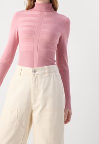 Pull col roulé rose ajusté avec un motif côtelé horizontal et manches longues, associé à un pantalon crème ample avec poches latérales.