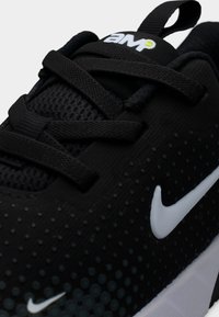 Μαύρο αθλητικό παπούτσι με λευκά λογότυπα Nike swoosh, μαύρα κορδόνια, υφασμένο επάνω μέρος και σήμανση «AMP» στον βρόγχο της γλώσσας.