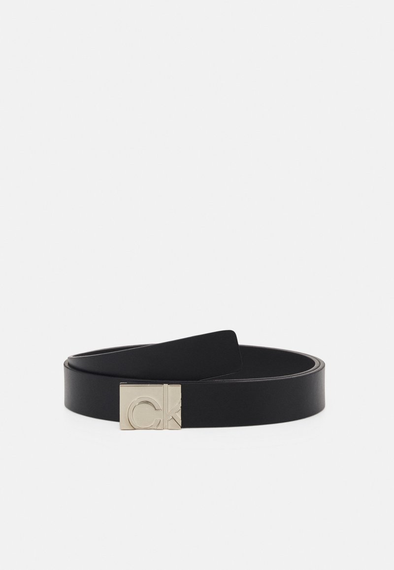 Ceinture en cuir noir avec boucle rectangulaire argentée présentant un logo "CK" en relief, montrée enroulée sur un fond gris clair.