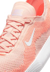 Heledad roosa sneaker, millel on tekstureeritud pealis, kontrastset valget Nike logot ja lapikud paelad. Pehme materjal ja kergesti kantav disain.