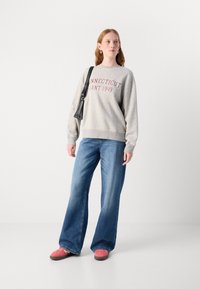 Šedá mikina s potiskem "CONNECTICUT GANT 1949" v maroon barvě, doplněná širokými modrými džíny a růžovými botami. Akcent v podobě černé kabelky.