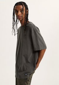 Přesně padnoucí šedé tričko z bavlny s krátkými rukávy, kulatým výstřihem a jemnou texturou. Na spodním lemu se nachází malá štítek značky.