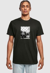 Camiseta negra con un gráfico central de una cancha de baloncesto detrás de una valla de eslabones de cadena, con el lema "NO ES SOLO UN JUEGO" debajo.