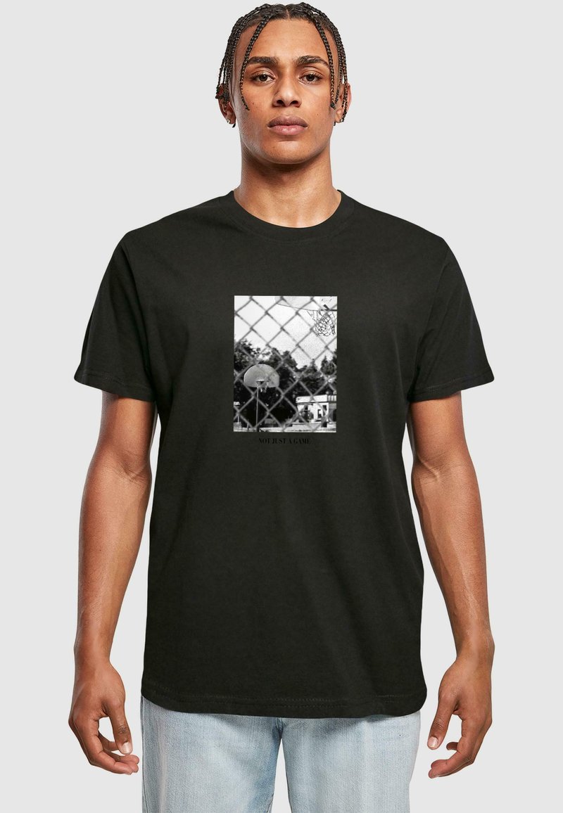 Camiseta negra con un gráfico central de una cancha de baloncesto detrás de una valla de eslabones de cadena, con el lema "NO ES SOLO UN JUEGO" debajo.