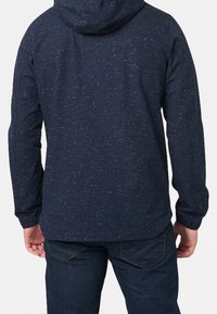 Mörkblå hoodie med en prickig textur, långa ärmar och en känguruficka, visad bakifrån. Justerbar huva ingår.