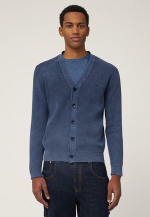 Navy ribbed cardigan with a V-neck, six buttons, and textured fabric. Worn over a blue crew-neck shirt, paired with dark jeans.
