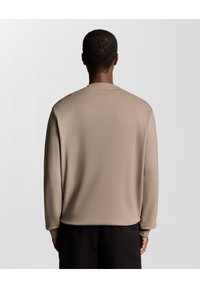 Beige langærmet skjorte med rund halsudskæring og glat tekstur, med afslappede skuldre og lige pasform, set fra ryggen.