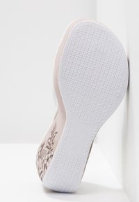Semelle d'une chaussure rose clair avec une semelle en caoutchouc blanche texturée, motif floral sur le côté et marquages de taille visibles sur la semelle.