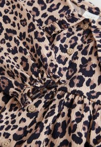 Obleka z leopardjim vzorcem v bež in temno rjavi barvi, z teksturirano tkanino, gumbnimi detajli ter nabranim pasom za poudarjen kroj.