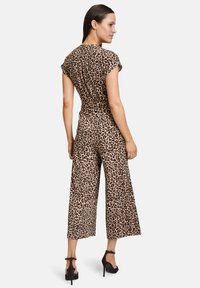 Overall s leopardím vzorom s krátkymi rukávmi, priliehajúcim pásom, širokými nohavicami po členky a hladkou tkaninou. Nosí sa s čiernymi sandálmi na vyššom opätku.