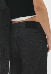 Zwarte denim jeans hebben een strak ontwerp met een donkere wassing, contrasterende stiksels en een subtiele rode accenten nabij de achterzakken.