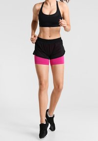 Top deportivo negro con escote redondeado, combinado con pantalones cortos negros que tienen bandas de acento rosas. Tejido texturizado y zapatillas deportivas.