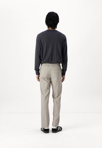 Chemise à manches longues gris foncé avec un col rond, associée à un pantalon gris clair à taille élastique. Des chaussures noires complètent la tenue.