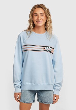 Světlo modra jopa z dolgimi rokavi, z rebrastimi manšetami in oranžno-črnim grafičnim motivom na prsih. Kombinirana z jeans kratkimi hlačami.