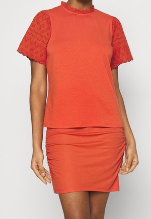 Rød top med ensfarvet krop, voluminøs krave og korte ærmer, der har detaljeret hullet lace. Sammen med en matchende, rynket mini nederdel.