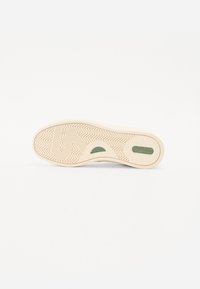 Sneaker outsole in cream rubber with a herringbone pattern. Features green accents and cutouts for flexibility. Clean, minimalist design.