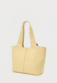 Μαλακή κίτρινη δερμάτινη τσάντα ώμου με φαρδιά διπλή λαβή και κεντρική κάθετη ραφή, εμφανιζόμενη σε απλό λευκό φόντο.