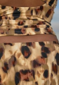 Tkanina z leopardjim vzorom v odtenkih porjavelosti, rjave in črne. Ima subtilne naborke in majhen zlat emblem na pasu.